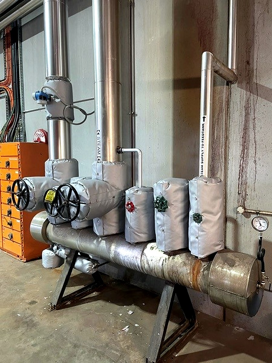 Thermal jackets on valve assemblies along a steam supply line with pressure gauges visible
